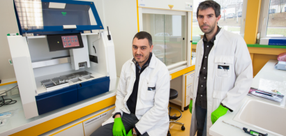 Paul Peixoto et Eric Hervouet, en blouse blanche, posent devant un robot d'immunoprécipitation.