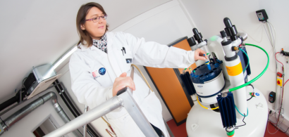 Une femme en blouse en train d'insérer un tube à essai dans un appareil de spectroscopie RMN