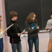 Un groupe de lycéens, garçons et filles, tenant des feuilles devant un tableau. L'un parle dans un micro.