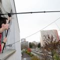 Un jeune homme penché à la fenêtre tient une perche au bout de laquelle est fixée un micro dans un environnement urbain.